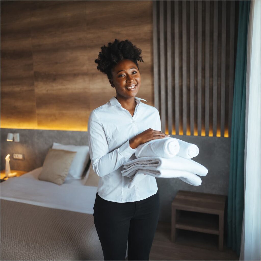 A smiling hotel housekeeper holding a stack of fresh white towels in a luxury guest suite at Ein Gedi Premier.